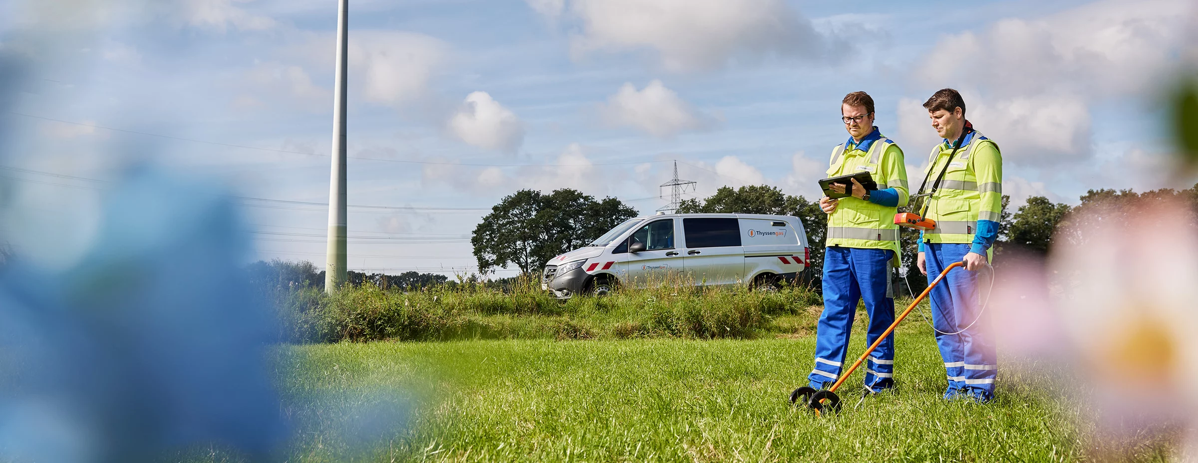 Zwei Thyssengas-Techniker bei der Trassenvermessung einer Gasleitung auf einer Wiese mit Service-Fahrzeug.