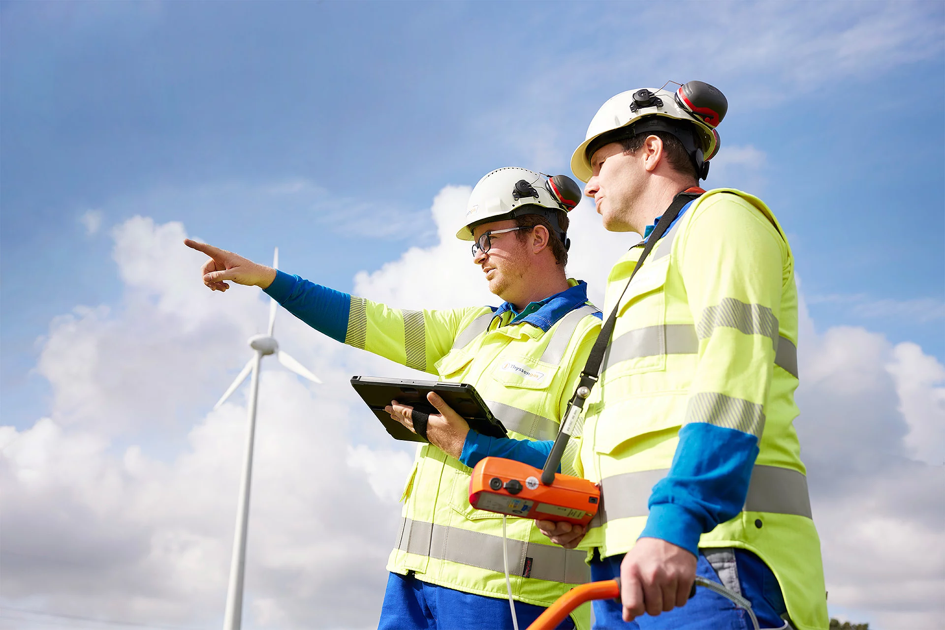 Zwei Thyssengas-Mitarbeiter mit Messtechnik vor einer Windkraftanlage, Symbol für den zukünftigen Energietransport.