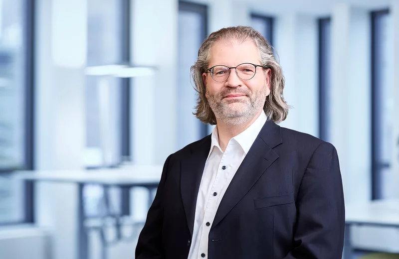 Portrait vom Thyssengas-Mitarbeiter Joachim Böhm mit Brille und Anzug vor einem modernen Bürohintergrund.