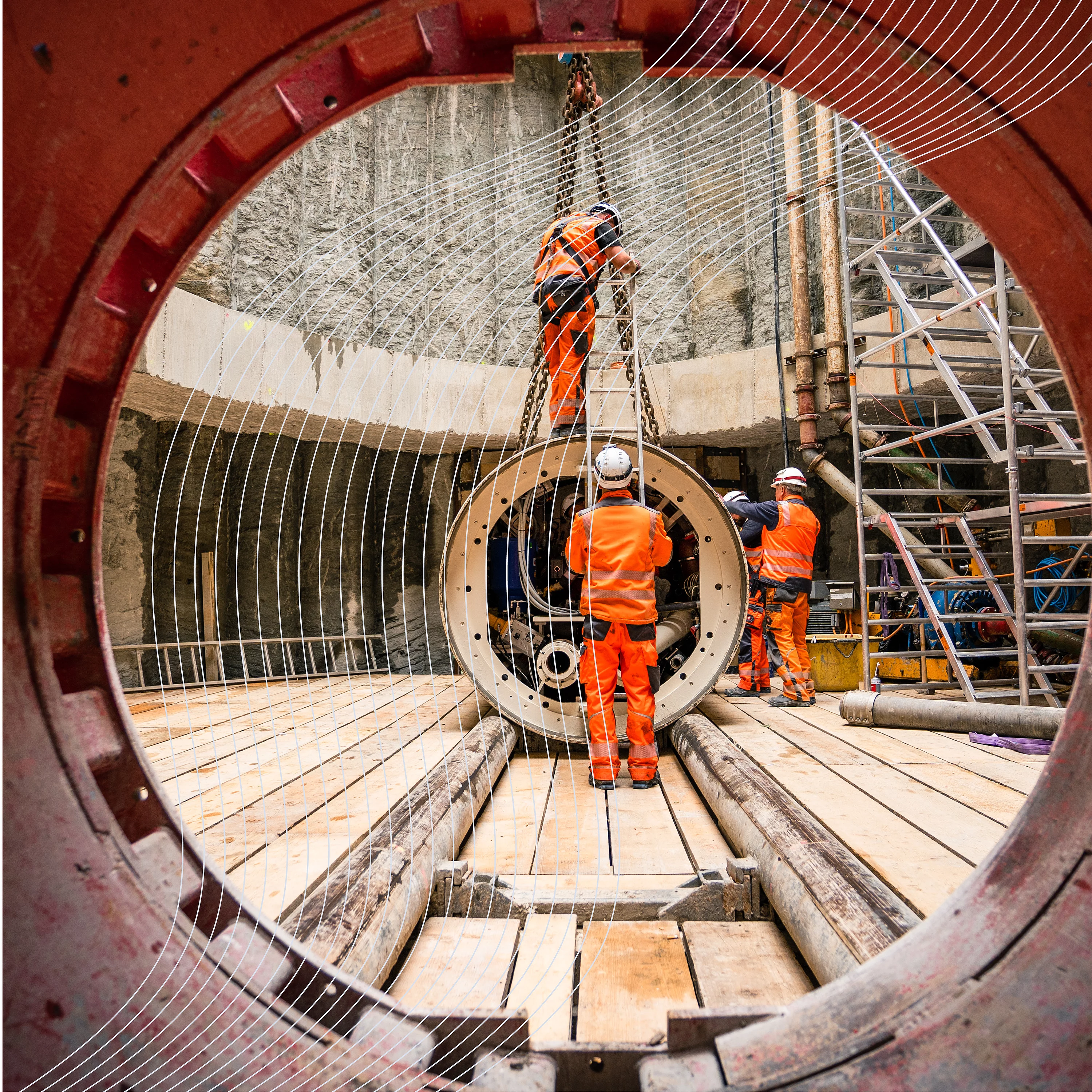 Blick durch ein Rohr auf den Bau einer Pipeline: Monteure installieren ein großes Leitungssegment in einer Baugrube.