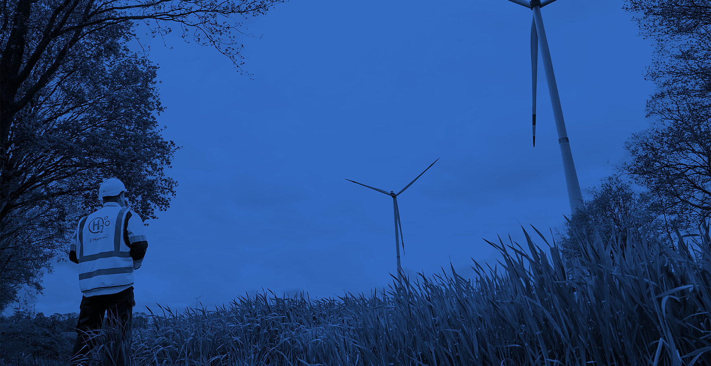 Blau getöntes Bild: Thyssengas-Mitarbeiter blickt auf Windräder, Symbol für den Transport von Wasserstoff (H2).