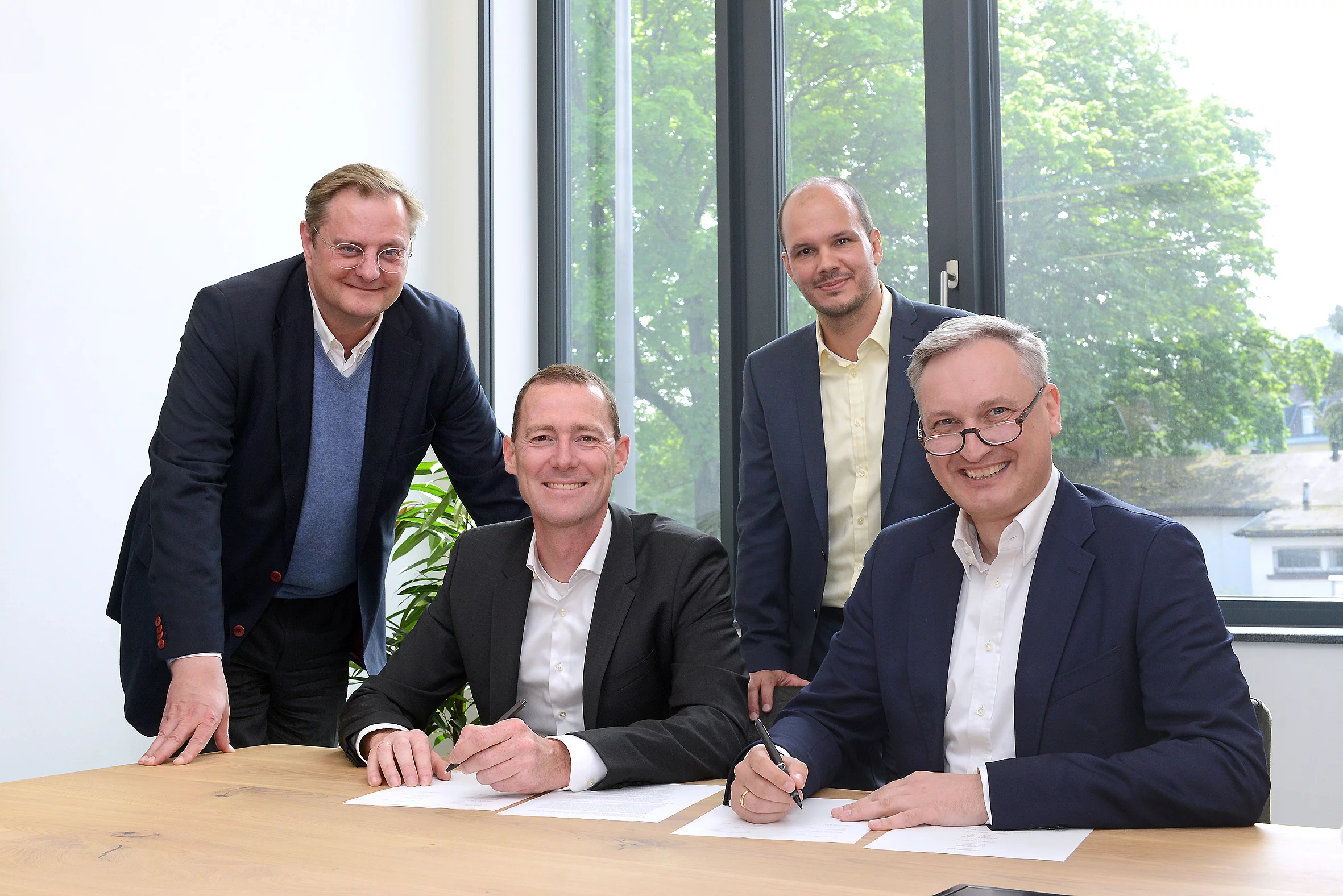 Vier Geschäftspartner bei der Vertragsunterzeichnung an einem Konferenztisch in einem modernen Büro.