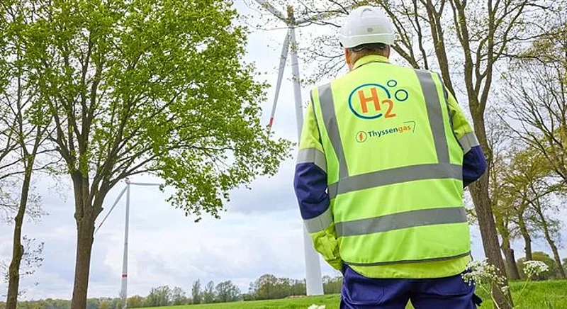 Thyssengas-Mitarbeiter mit H2-Logo auf der Weste blickt auf Windräder, Symbol für Jobs in der Energiewende.