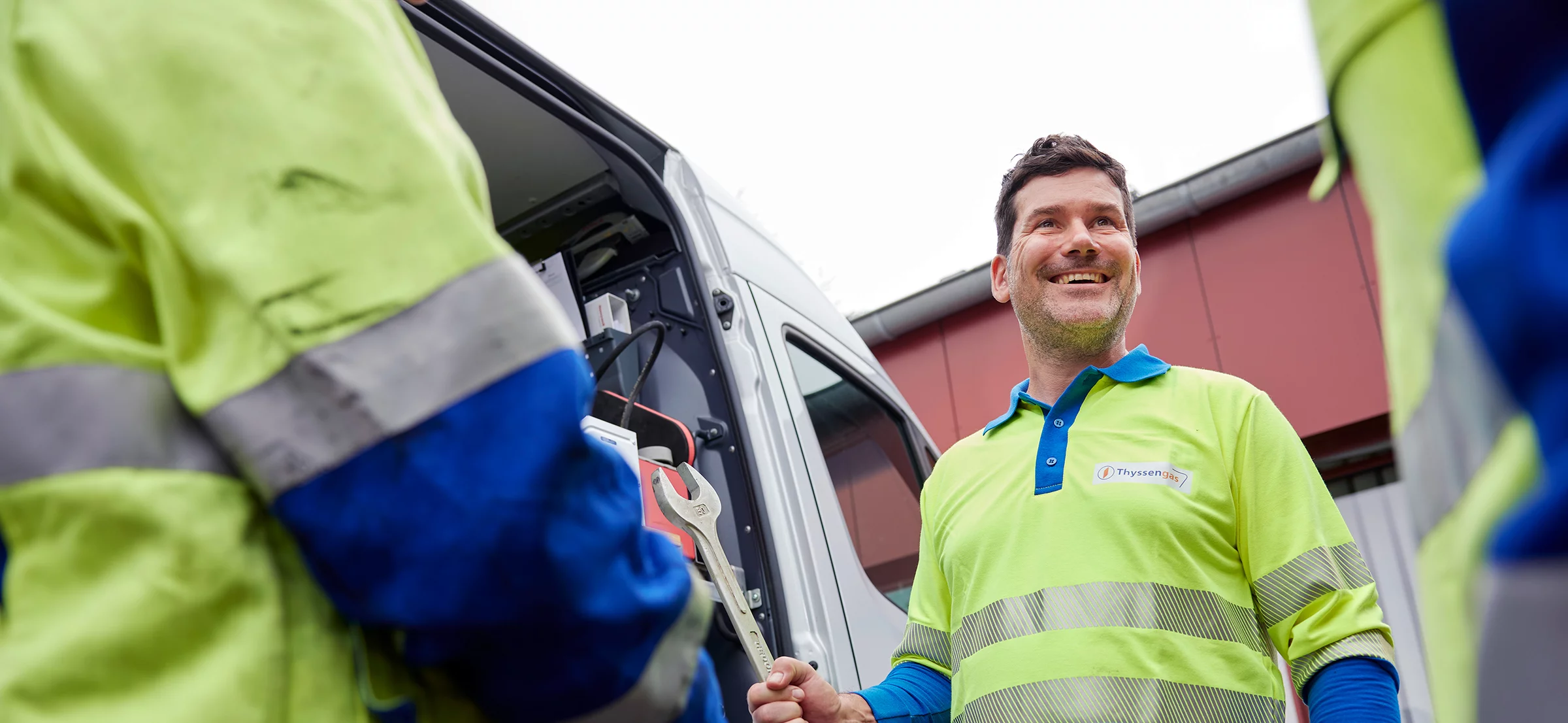 Lächelnder Thyssengas-Monteur in Schutzkleidung mit Werkzeug vor einem Service-Fahrzeug im Einsatz.
