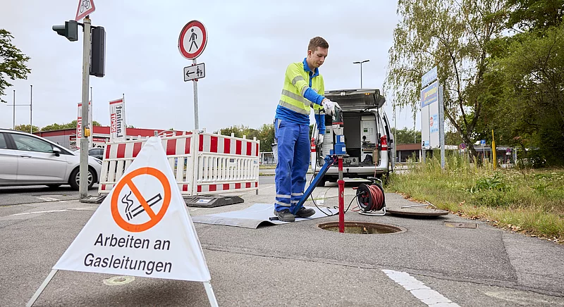 Thyssengas-Techniker bei Arbeiten an einer Gasleitung mit Warnschild und geöffnetem Kanalschacht an einer Straße.