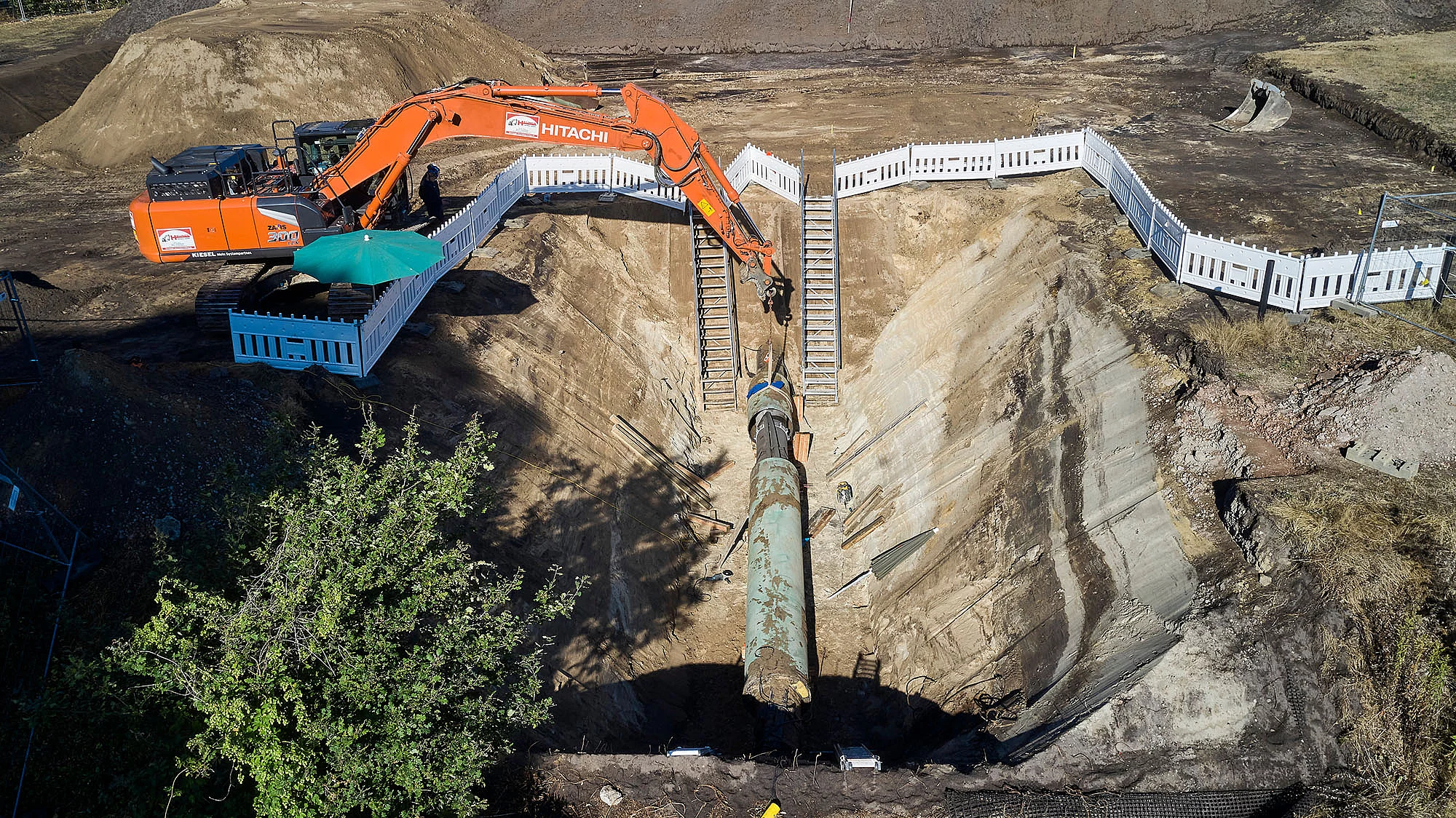 Luftaufnahme einer Baustelle: Ein Bagger verlegt eine große Pipeline für das zukünftige Wasserstoffnetz.