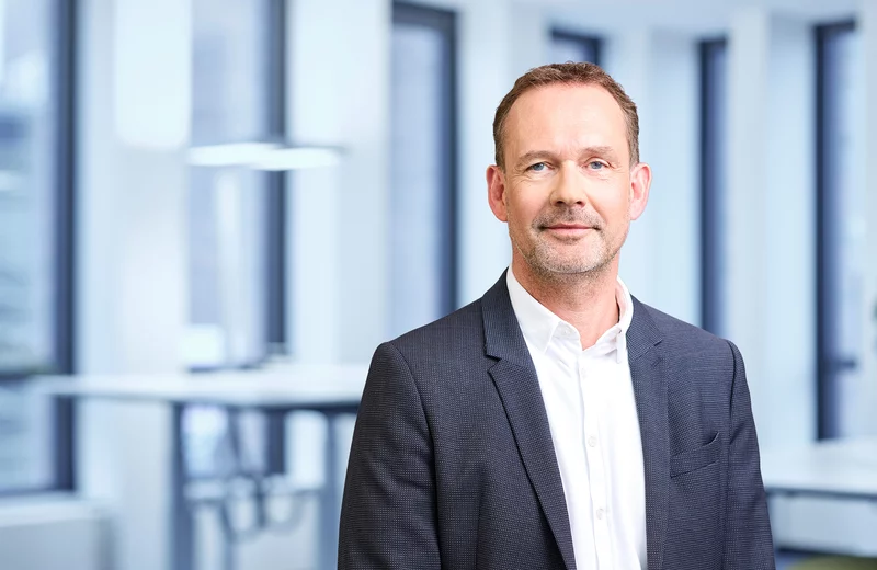 Portrait vom Thyssengas-Mitarbeiter Gregor Seidewinkel in grauem Anzug und weißem Hemd vor modernem Bürohintergrund.