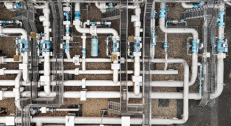 Luftaufnahme einer Gas-Verdichterstation: Dichtes Netz aus Rohrleitungen, Armaturen und Gitterrosten von oben.