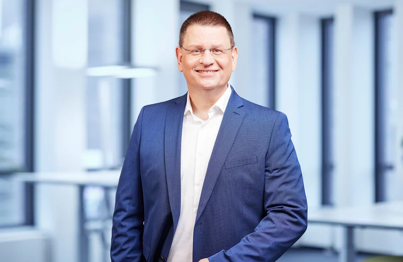 Portrait von Thyssengas-Mitarbeiter Mike Sawitzki in blauem Anzug vor modernem Bürohintergrund.