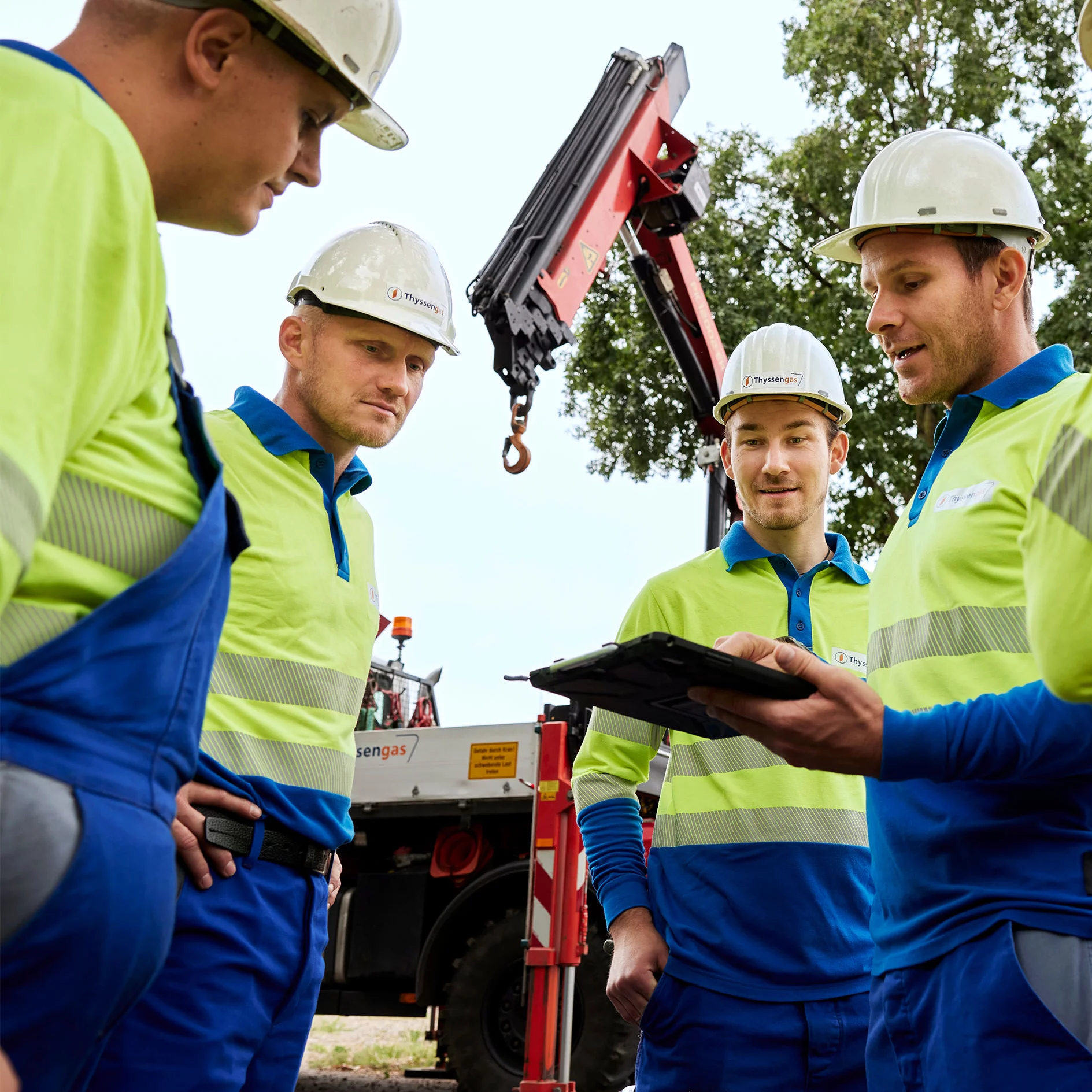 Fünf Thyssengas-Mitarbeiter in Arbeitskleidung stehen in einem Kreis zusammen und schauen es etwas auf einem Tablet an.