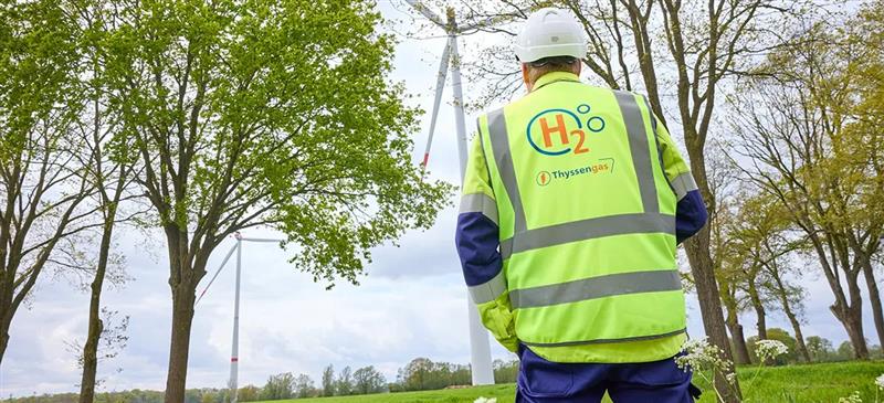 Thyssengas-Mitarbeiter mit H2-Logo auf der Weste blickt auf Windräder, Symbol für Jobs in der Energiewende.
