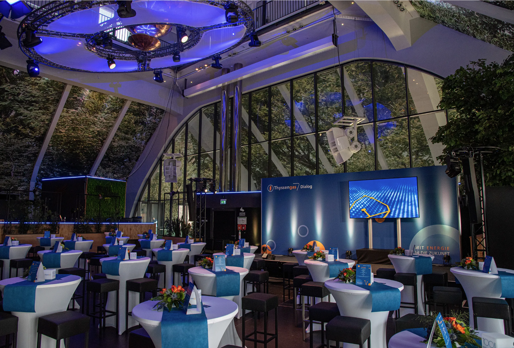 Modern eingerichteter Veranstaltungsraum für den Thyssengas Dialog mit Bühne und blau-weißen Stehtischen.
